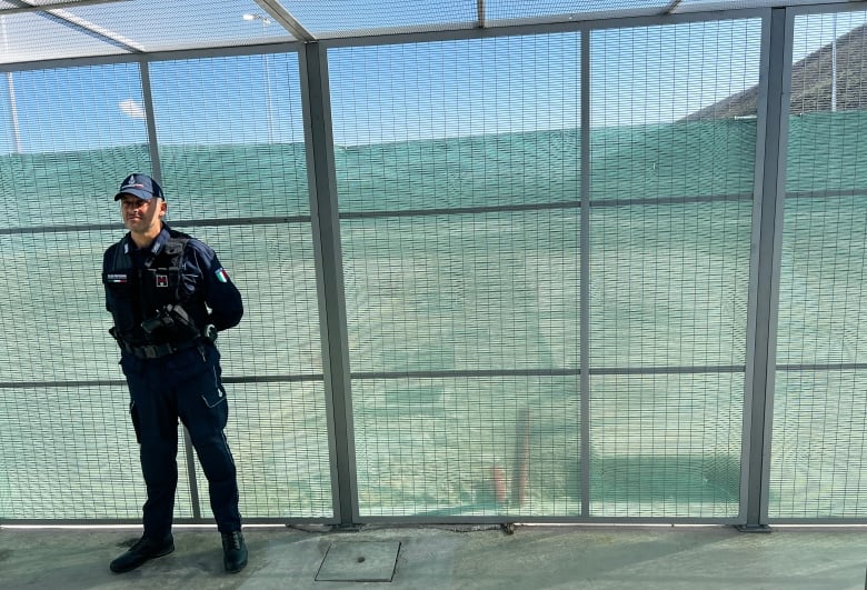 A man in a blue guard's uniform stands in front of a tall fence.