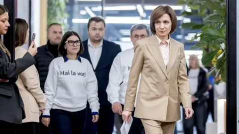 EPA Wearing a beige suit with short, chin-length brown hair, the president of Moldova walks in front of her entourage, carrying a sheet of A4 paper in her right hand