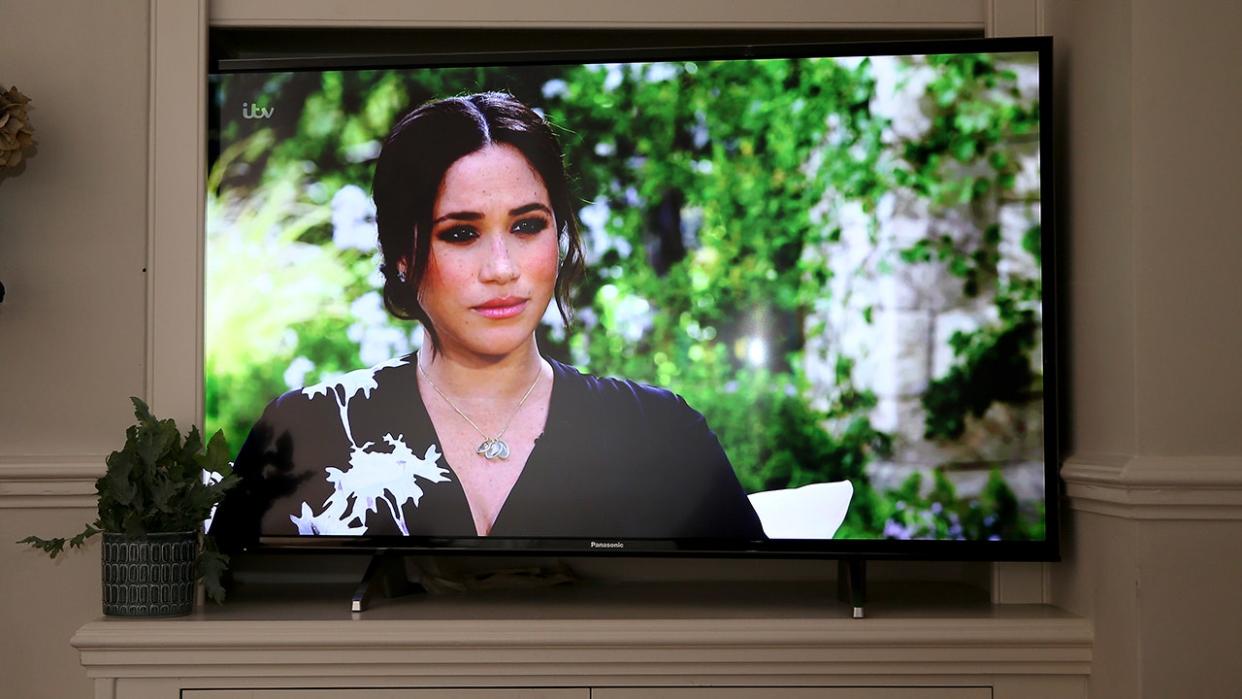 Meghan Markle in a black and white floral dress speaking from a TV screen.