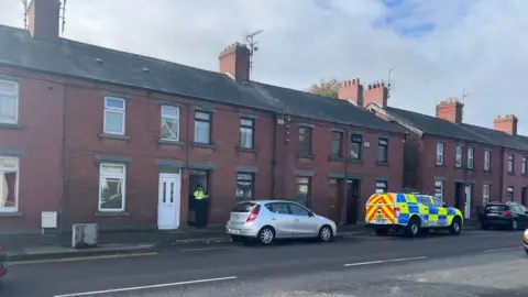 A uniformed garda officer stands inside the entrance of a red brick terraced house in Emer Terrace Dundalk during the search for Kyran Durnin.