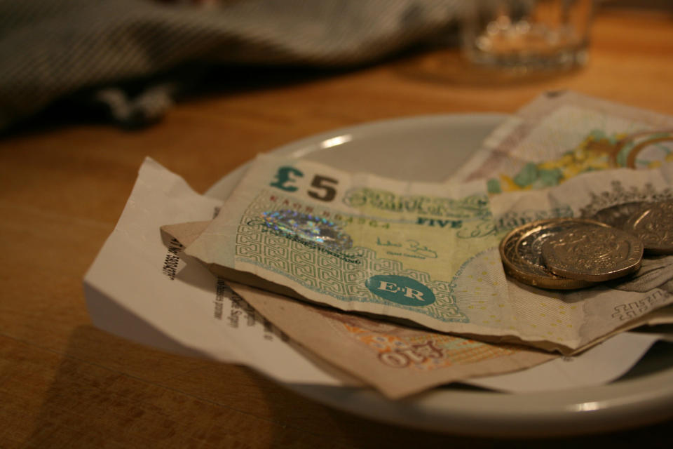 Currency notes and coins placed on a small white dish on a wooden table, likely used for payment or a tip