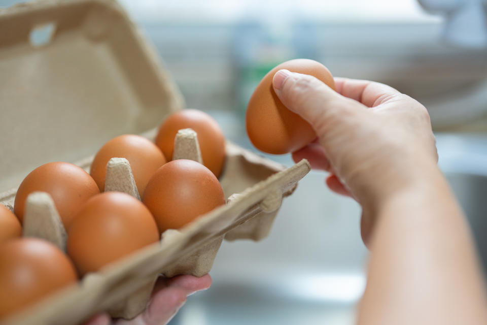 Person's hand holding an egg from a carton in a kitchen setting