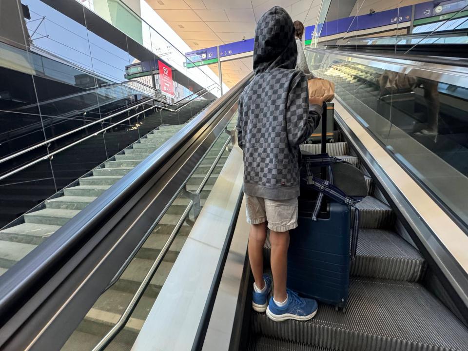 child holding a suitcase and duffle bag on an escalator in a train station