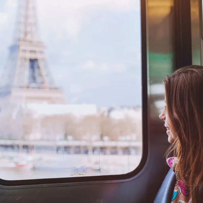 a woman riding a train looks out the window to see the Eiffel tower