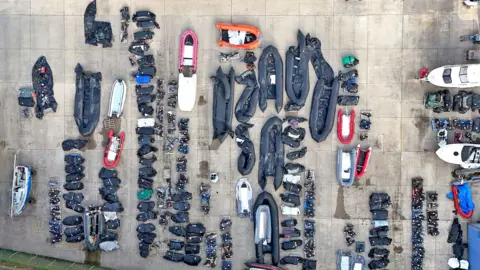 Gareth Fuller/PA Wire A view from above of small boats and outboard motors in various states of disrepair used by people thought to be migrants to cross the Channel at a warehouse facility in Dover, Kent. 