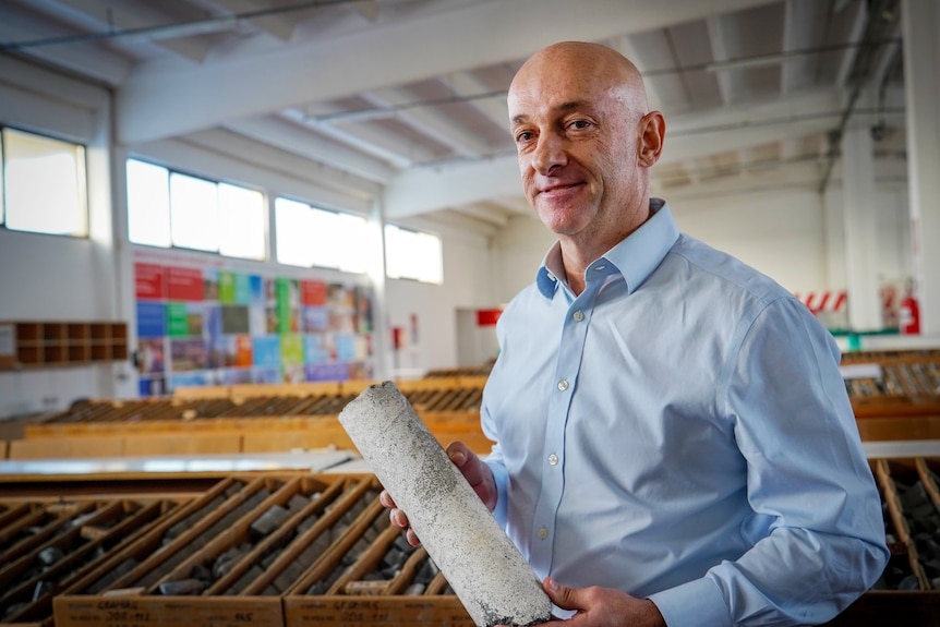 A man holding an object looks at the camera and smiles.