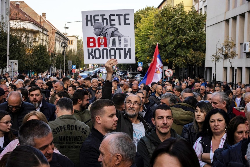 A large number of people on a street, including one holding a sign