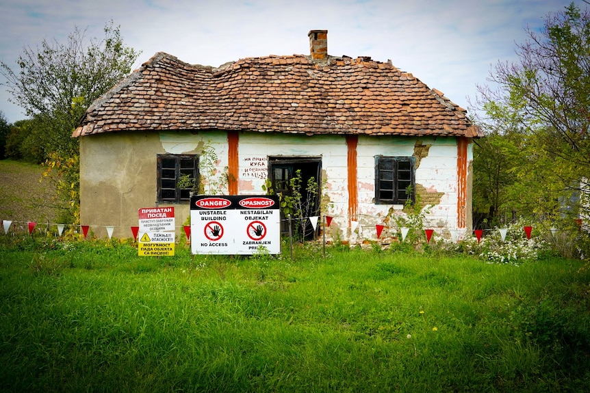 A rundown house, surrounded by warning signs.