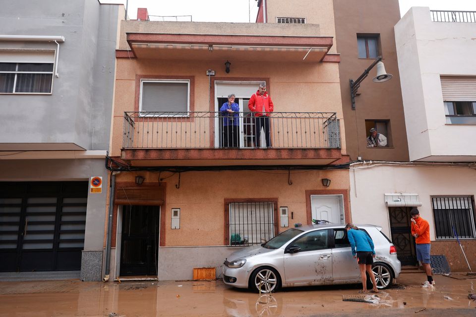 People inspect a damaged car on a mud-covered street after torrential rains caused flooding in La Alcudia, Valencia region, Spain, October 30, 2024. REUTERS/Eva Manez