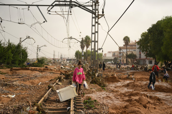 A woman walks along train tracks covered debris after flash-flooding hit the Valencia region.