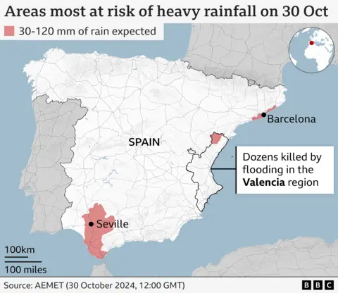 Map showing the areas most at risk of heavy rainfall in Spain, highlighting the cities of Barcelona and Seville. The region of Valencia is also highlighted. A label says that dozens were killed by flooding in the Valencia region