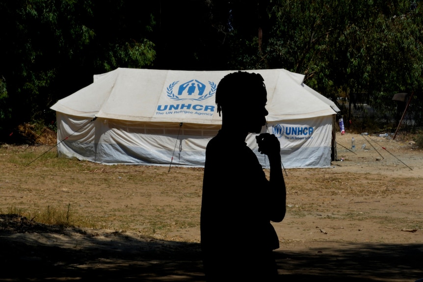 man silhouette standing infront of a white tent 