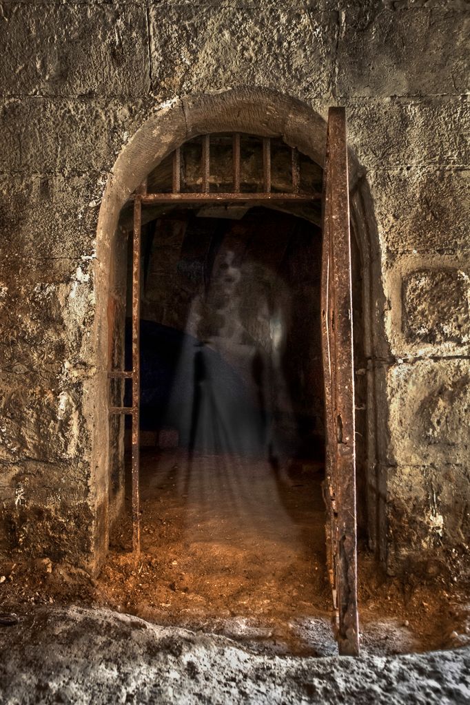 AN open cell inside medieval dungeons with an apparition inside