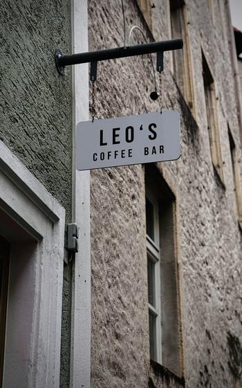 A white sign hangs outside with words for Leo’s Coffee Bar. 