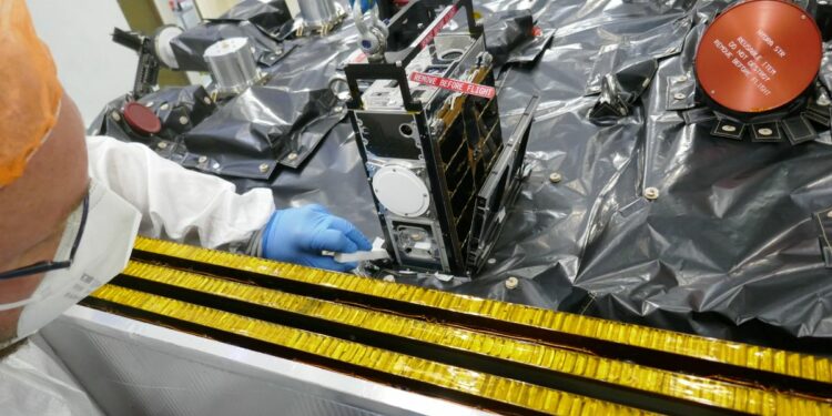 A metal rack of computer components are stacked in a cubesat on a table covered in a black tarp.