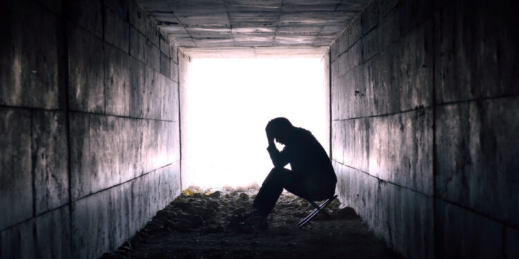 Black and white photograph of person sitting with head in hands in a dark tunnel.