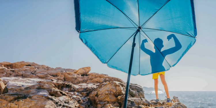 Silhouette of boy flexing his muscles on blue beach umbrella