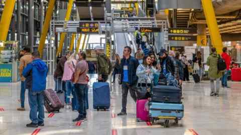 Passengers stand with luggage in the departures hall at Madrid Barajas airport