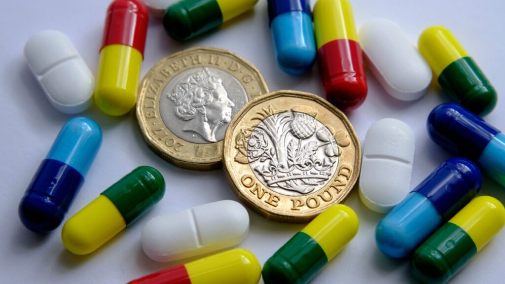 Pile of different colouful pills placed around two british pound coins. Illustrative for cost of medical bills, treatment, health insurance and other subjects