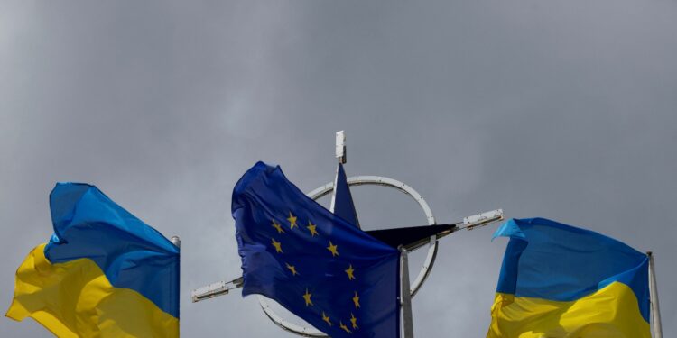 Two national flags of Ukraine flank the European Union flag in the foreground to the NATO emblem with storm clouds in the background in central Kyiv, Ukraine on July 11, 2023. REUTERS/Valentyn Ogirenko