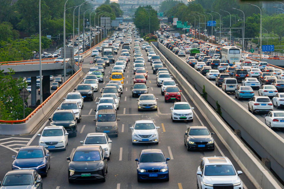 Aerial view of heavy traffic on a multi-lane highway in an urban area, surrounded by green trees and overpasses