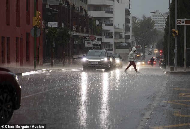 A passer-by walks across the street during a downpour in Palma on November 1