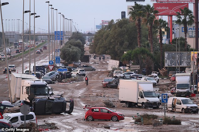 People walk by cars and trucks that were among the debris swept up in recent flash flooding along the V-31 highway near the municipality of Massanassa on November 1, 2024 on the outskirts of Valencia