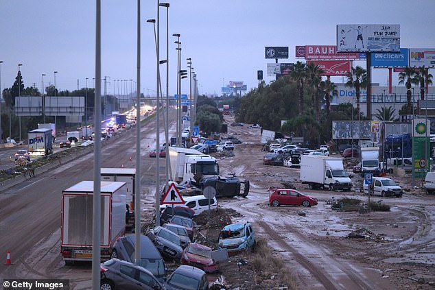 People walk by cars and trucks that were among the debris swept up in recent flash flooding along the V-31 highway near the municipality of Massanassa on November 1, 2024 on the outskirts of Valencia