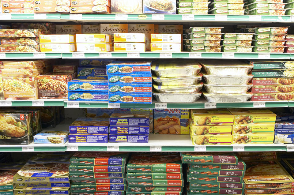 Grocery store freezer aisle displaying various packaged frozen meals and snacks stacked on shelves