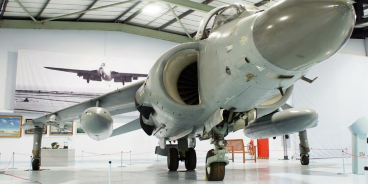 A white aircraft in a museum with a BAe Sea Harrier sign below it