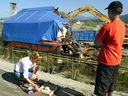 Unidentified family or friend lights a candle while another watches as a construction shovel demolishes the Pickton farm house on the pig farm in Port Coquitlam, B.C. Saturday July 26, 2003. The B.C. Supreme Court says it has jurisdiction to order the disposal of thousands of pieces of evidence seized from Robert Pickton's pig farm decades ago, whether it was used in his murder trial or not.