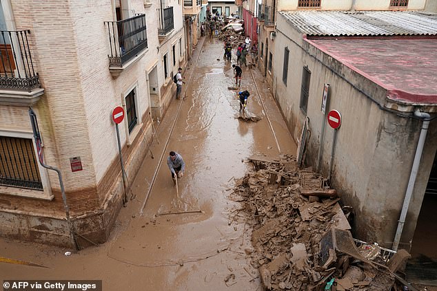 People try to drag mud on a street full of debris in Catarroja, region of Valencia