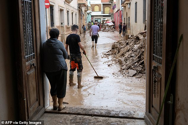 A woman at her home's entrance looks at people clening the streets in Catarroja, region of Valencia, eastern Spain