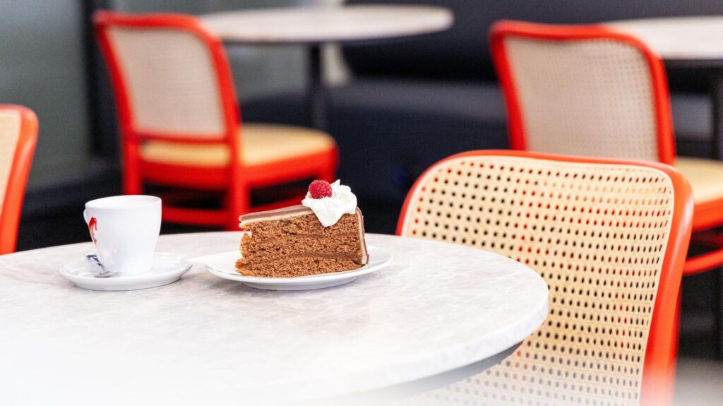A slice of cake sits on a table beside a cup of coffee.