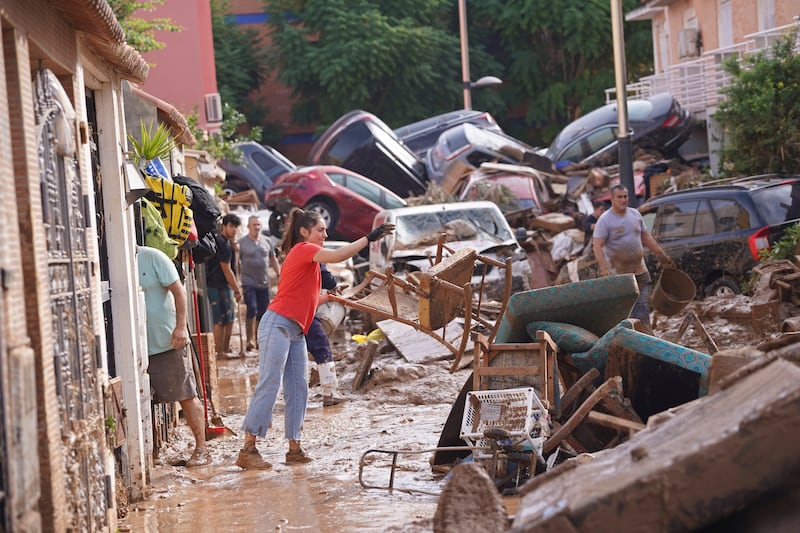 A woman throws a damaged chair into the street with other damaged furniture and cars.