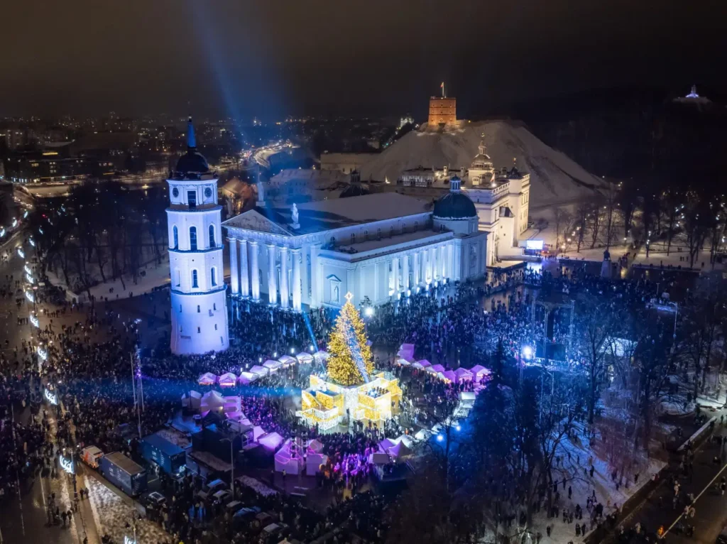 Aerial view of Vilnius’s Cathedral Square during Christmas, featuring a beautifully lit Christmas tree surrounded by festive markets and crowds.