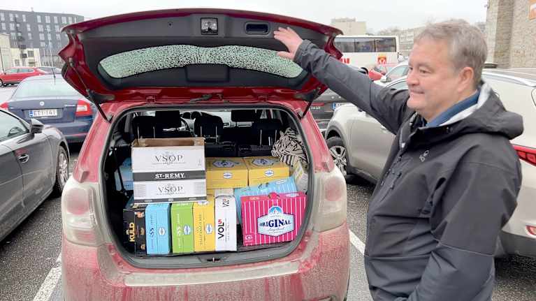Man standing at the rear of a station wagon which is filled with boxes of alcoholic beverages.