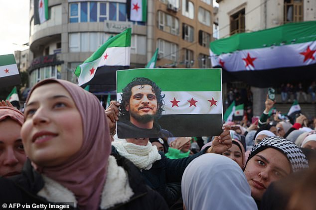 A woman lifts a flag of the Syrian revolution bearing a portrait of late rebel fighter and famous chanter Abdel-Basset al-Sarout during celebrations to mark this week's ouster of president Bashar al-Assad
