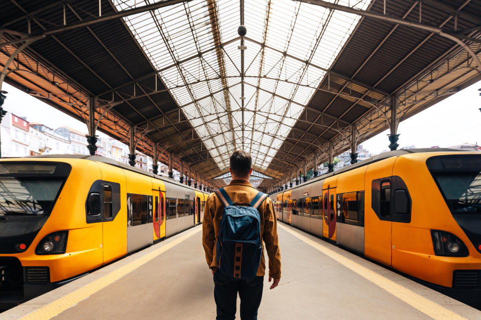 Person with a backpack stands between two trains in a spacious station, suggesting travel or transit