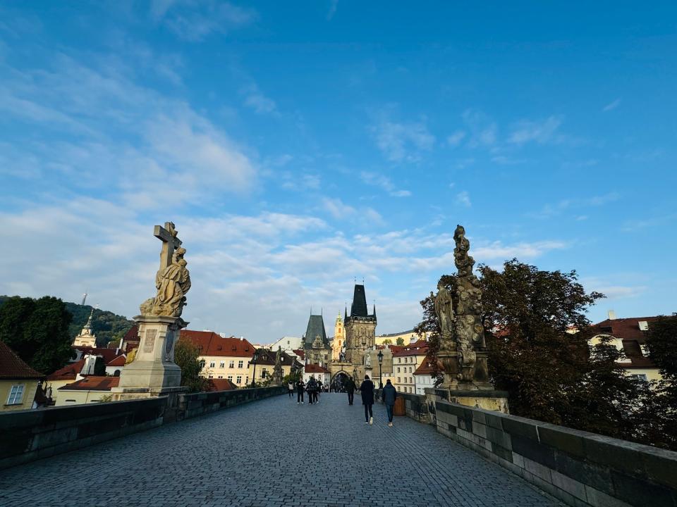 A few people walking across a bridge in Prague, with statues on each side.