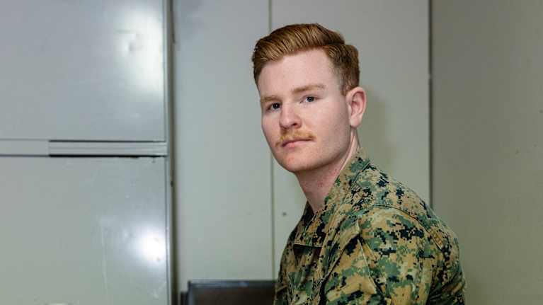 A man wearing a US Marine camouflage uniform looks towards the camera.