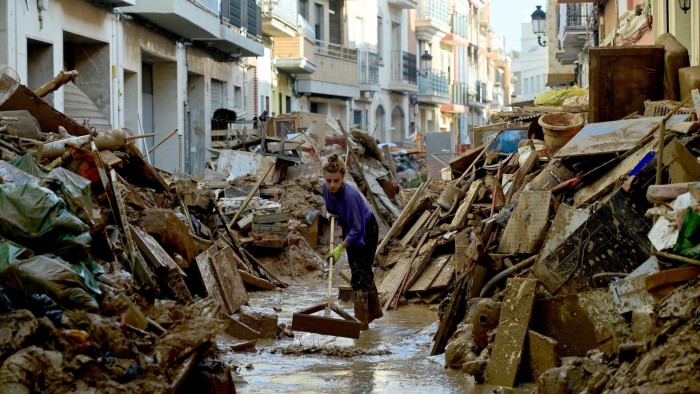 A woman works to clean mud among debris in a street of Paiporta, south of Valencia