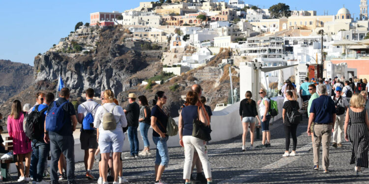 Countless tourists congest pathways while sightseeing and snapping pictures in Santorini, Greece.