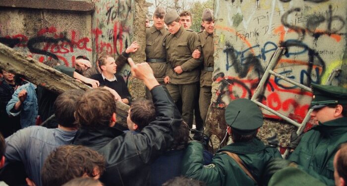 A group of West German demonstrators tear down a section of the Berlin Wall under the gaze of East-German border guards