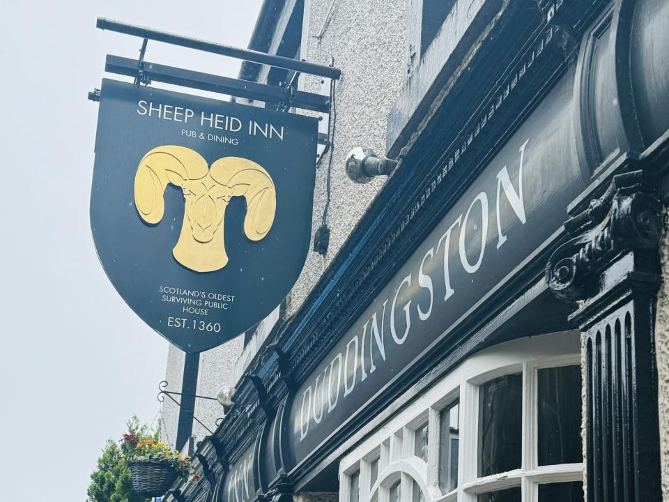 A black sign with a gold ram outside a pub that reads, 