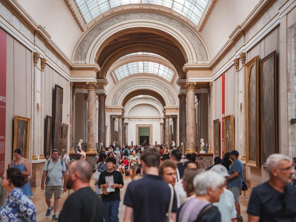 A crowd of people walk through a museum with a curved ceiling.