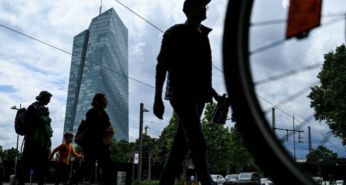 People cross a street in front the headquarters building of the European Central Bank