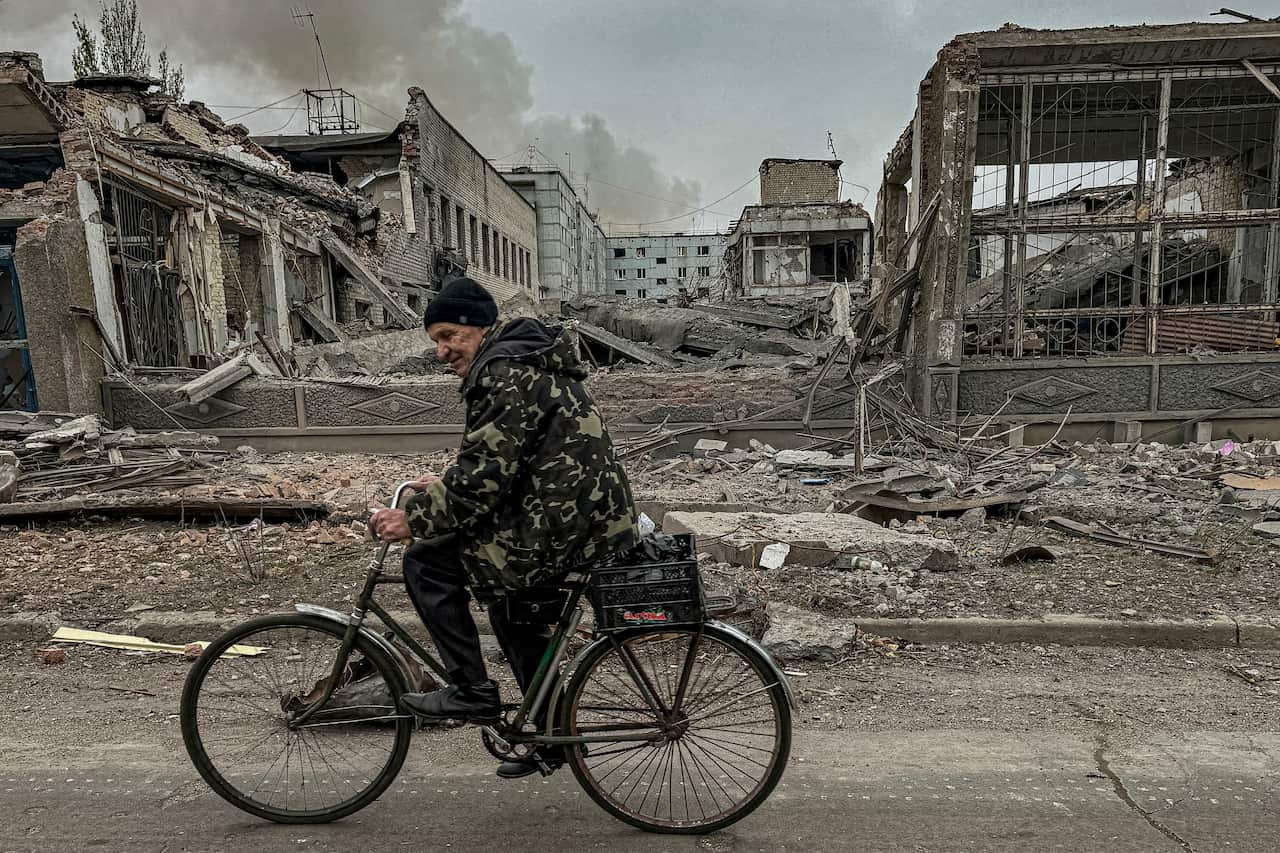 A man rides on a bike in front of a destroyed building.