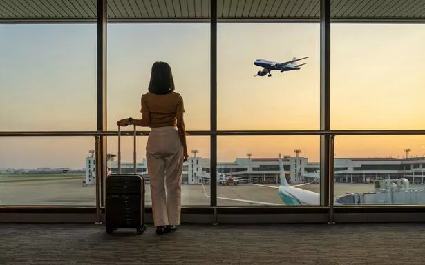 Travel tourist standing with luggage watching sunset at airport window