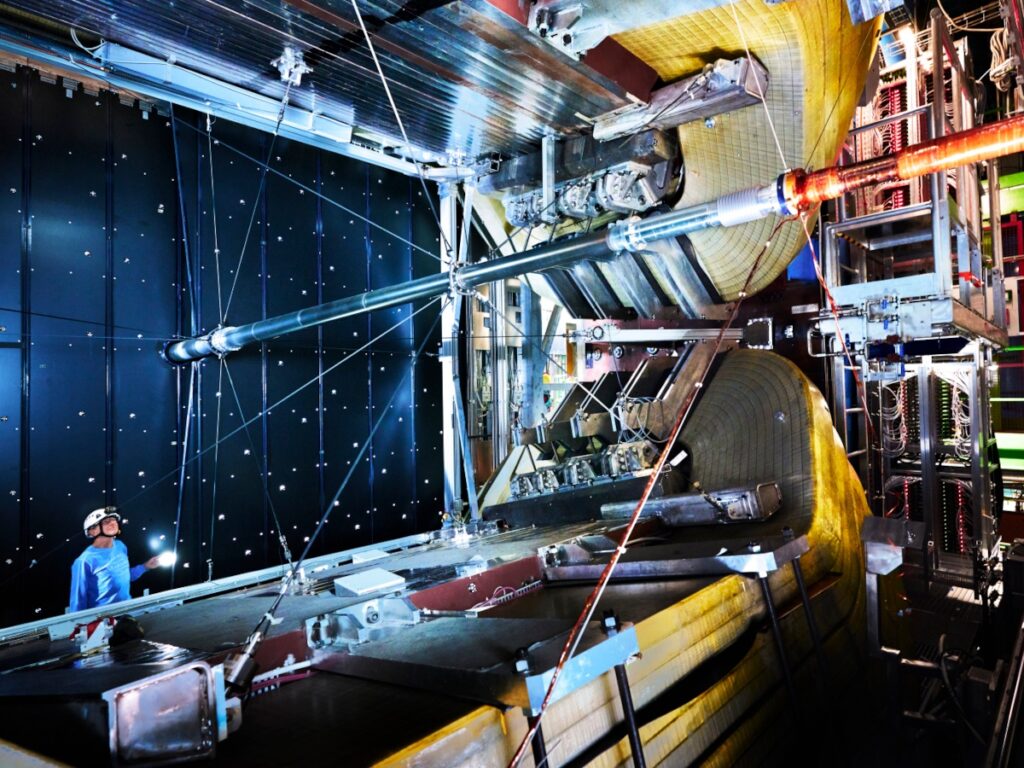 A man in a blue shirt and a safety helmet looking up at the Large Hadron Collider.